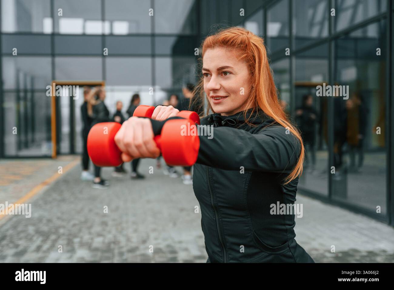 Tenendo i manubri. Un gruppo di donne sportive si trova all'aperto vicino all'edificio nero. Foto Stock