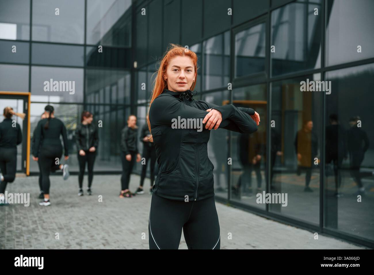 Esercizi di riscaldamento. Un gruppo di donne sportive si trova all'aperto vicino all'edificio nero. Foto Stock