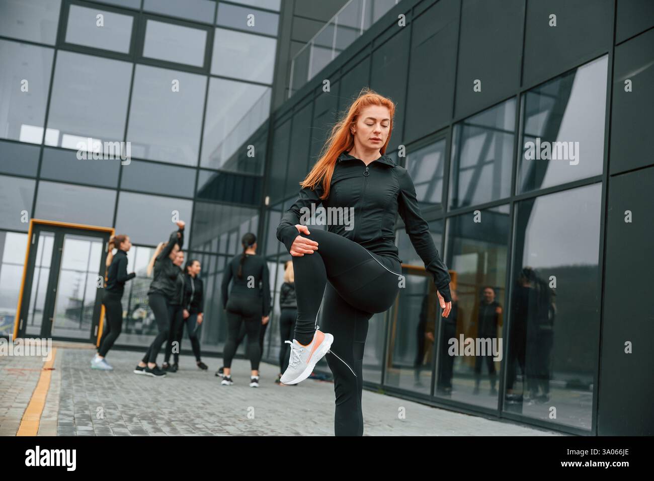 Esercizi di riscaldamento. Un gruppo di donne sportive si trova all'aperto vicino all'edificio nero. Foto Stock