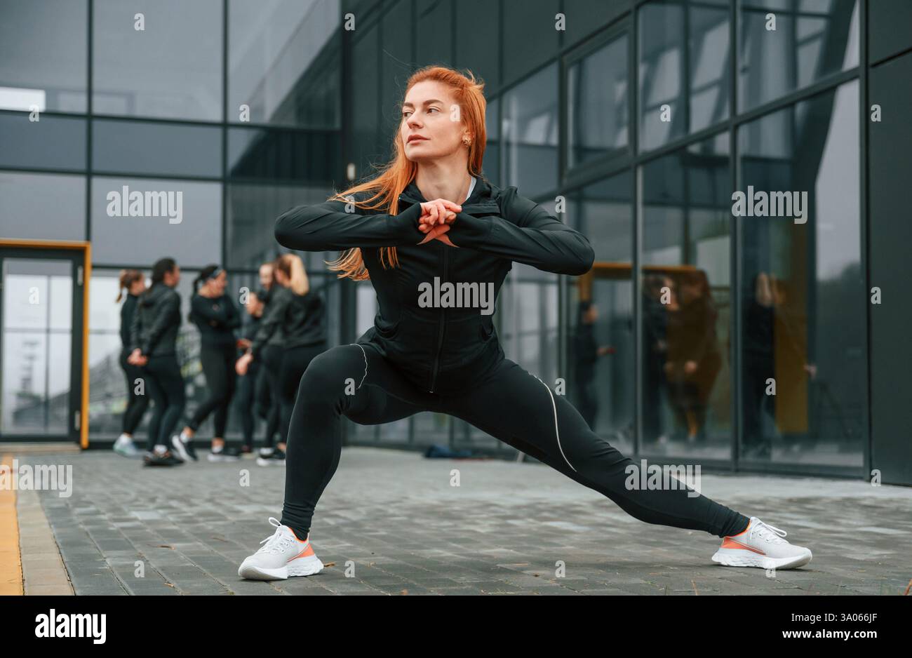 Fare esercizi di stretching. Un gruppo di donne sportive si trova all'aperto vicino all'edificio nero. Foto Stock