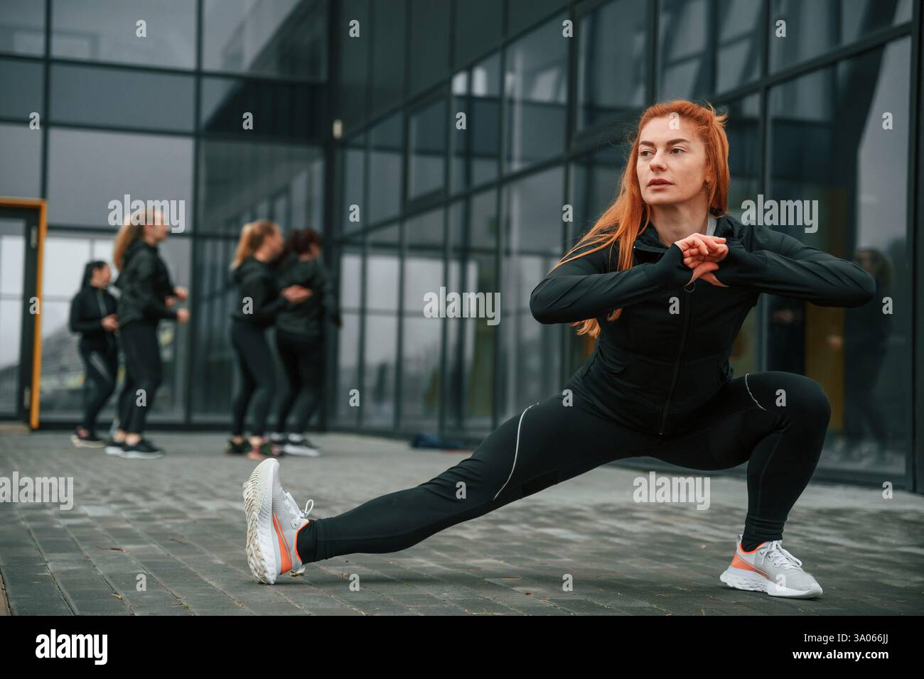 Fare esercizi di stretching. Un gruppo di donne sportive si trova all'aperto vicino all'edificio nero. Foto Stock