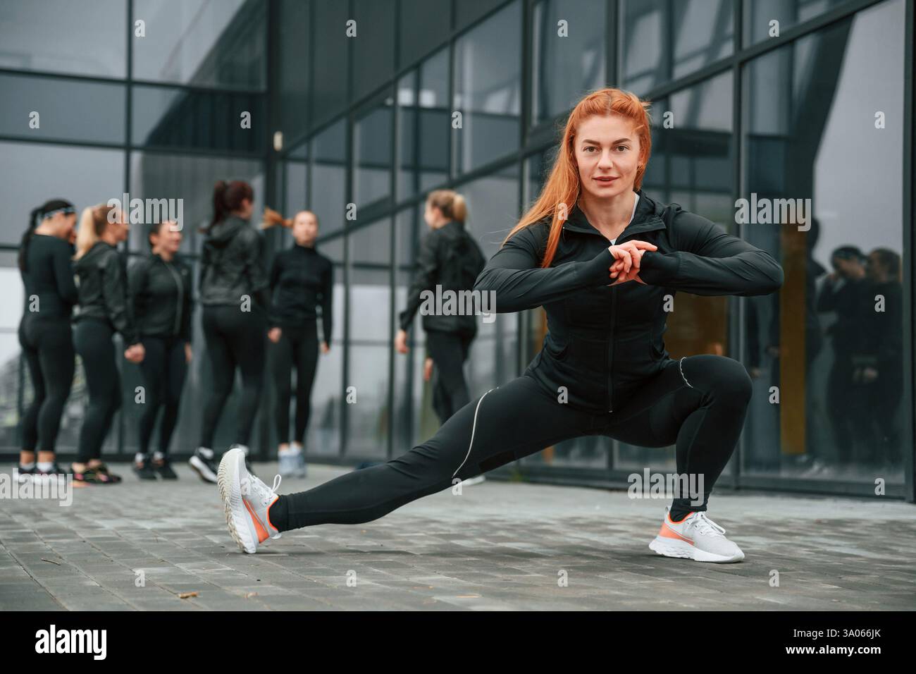 Fare esercizi di stretching. Un gruppo di donne sportive si trova all'aperto vicino all'edificio nero. Foto Stock