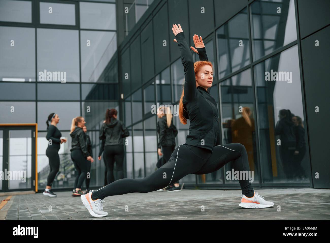 Fare esercizi di stretching. Un gruppo di donne sportive si trova all'aperto vicino all'edificio nero. Foto Stock