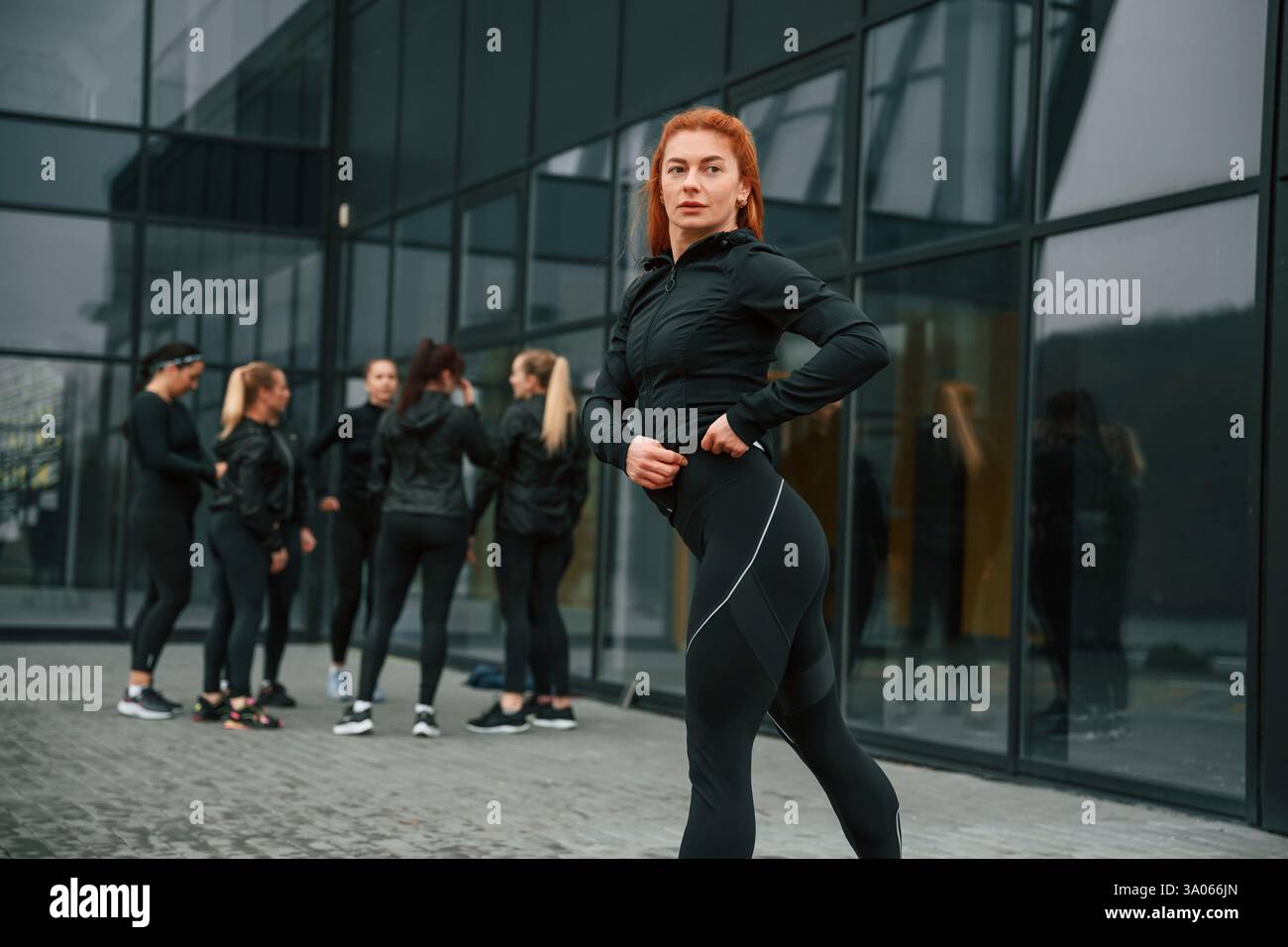Redhead si sta schierando contro i suoi amici. Un gruppo di donne sportive si trova all'aperto vicino all'edificio nero. Foto Stock