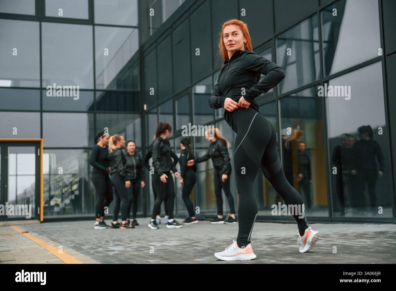 Redhead si sta schierando contro i suoi amici. Un gruppo di donne sportive si trova all'aperto vicino all'edificio nero. Foto Stock