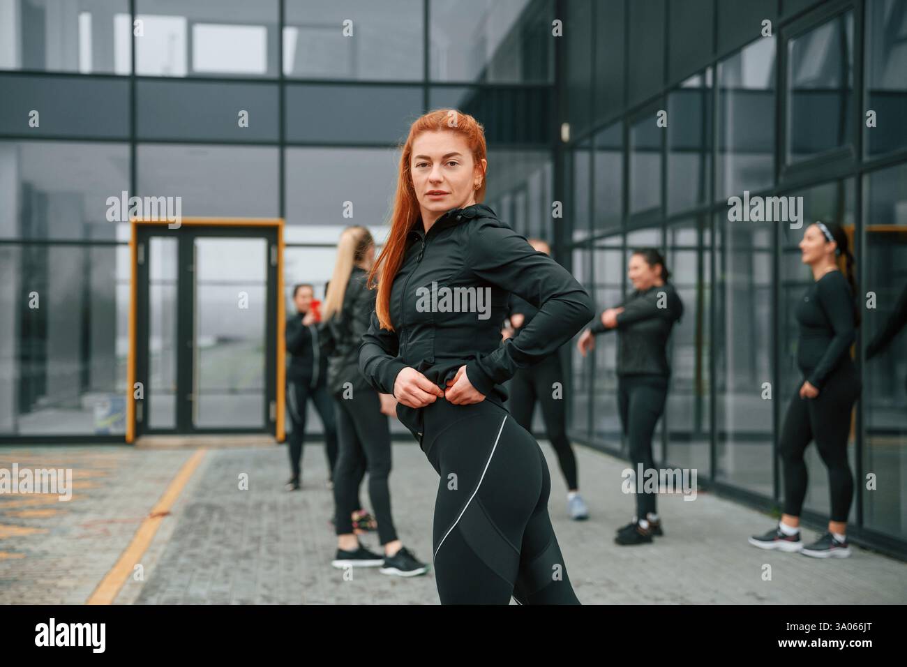 Redhead si sta schierando contro i suoi amici. Un gruppo di donne sportive si trova all'aperto vicino all'edificio nero. Foto Stock