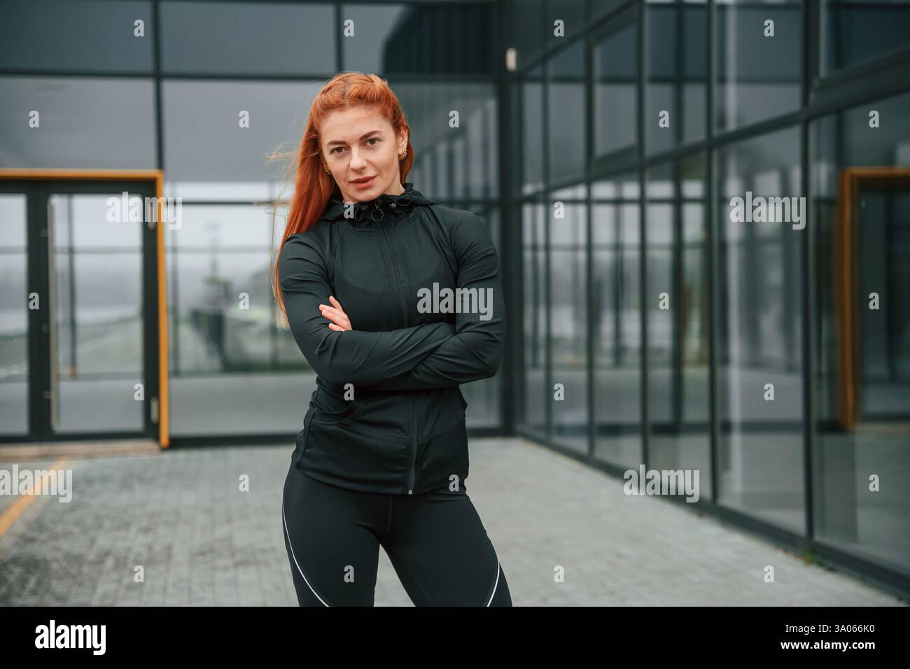 In piedi con le braccia incrociate. La donna è abbigliamento sportivo all'aperto contro l'edificio nero. Foto Stock