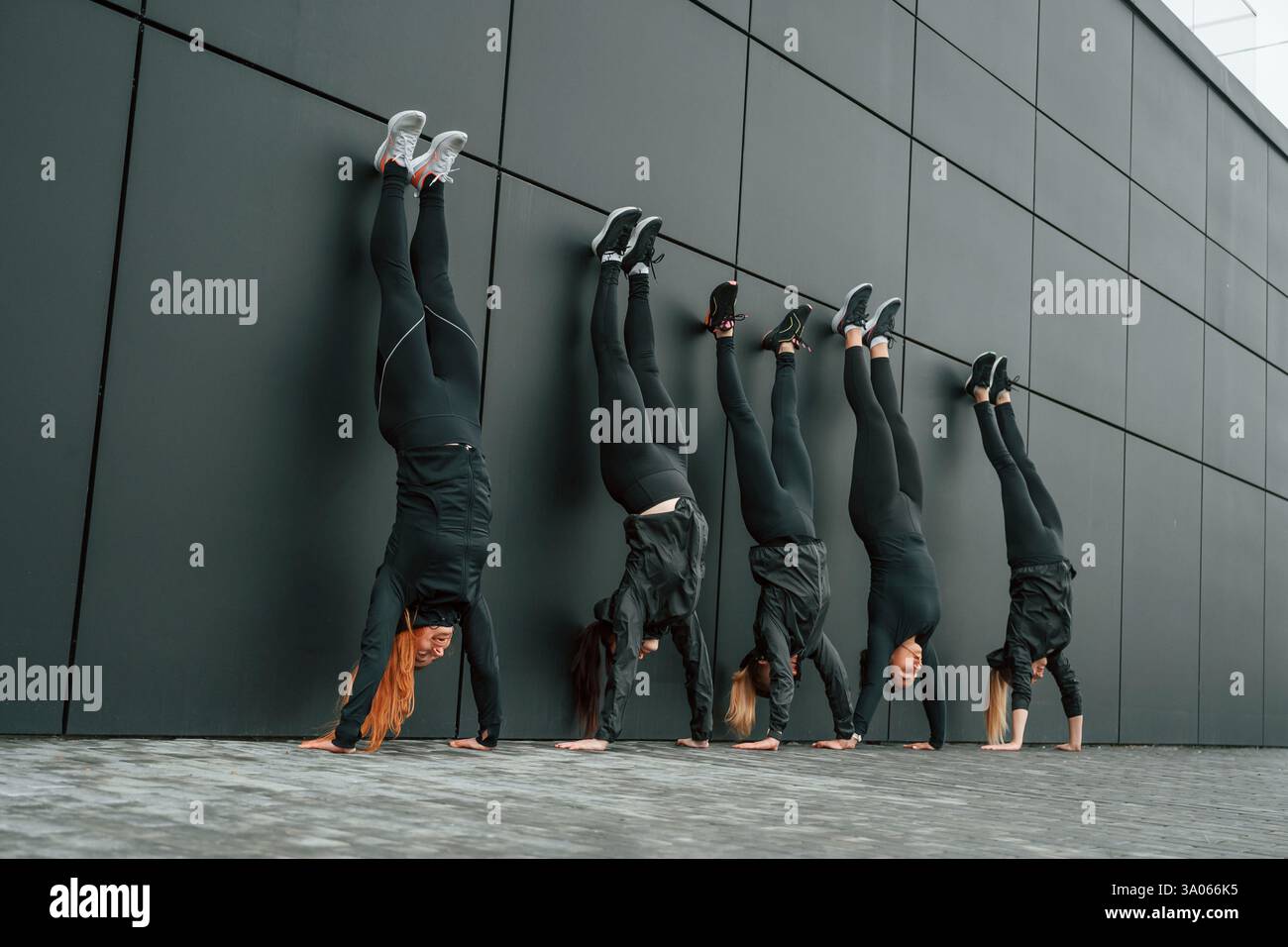 Sto facendo il supporto manuale. Un gruppo di donne sportive si trova all'aperto vicino all'edificio nero. Foto Stock