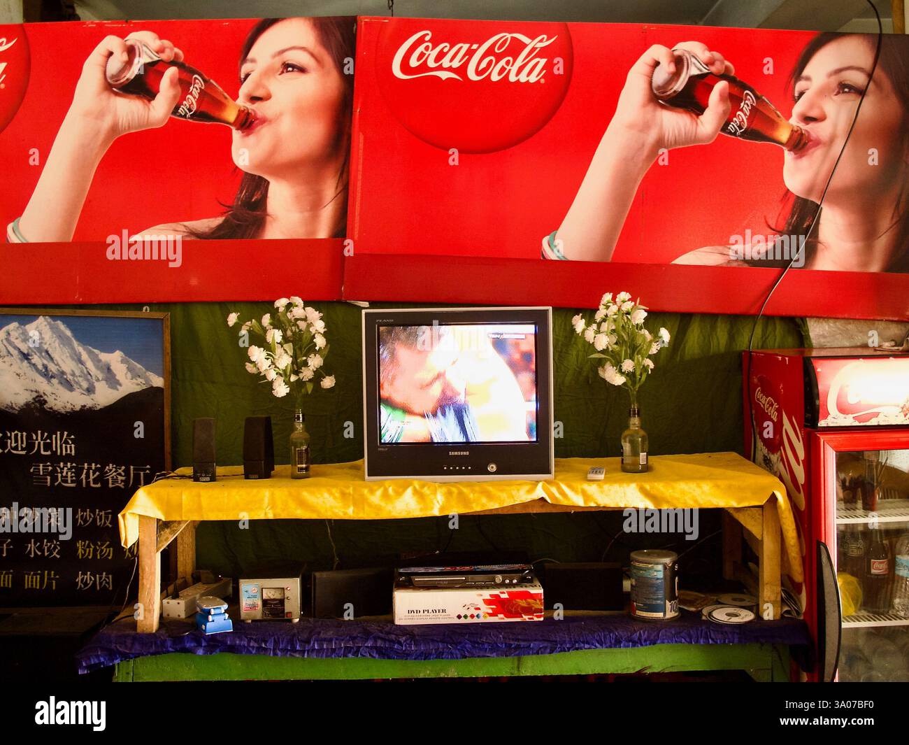 Pubblicità e decorazioni della Coca-Cola intorno a un televisore in un ristorante tibetano locale a Bodh Gaya, Bihar. Foto Stock