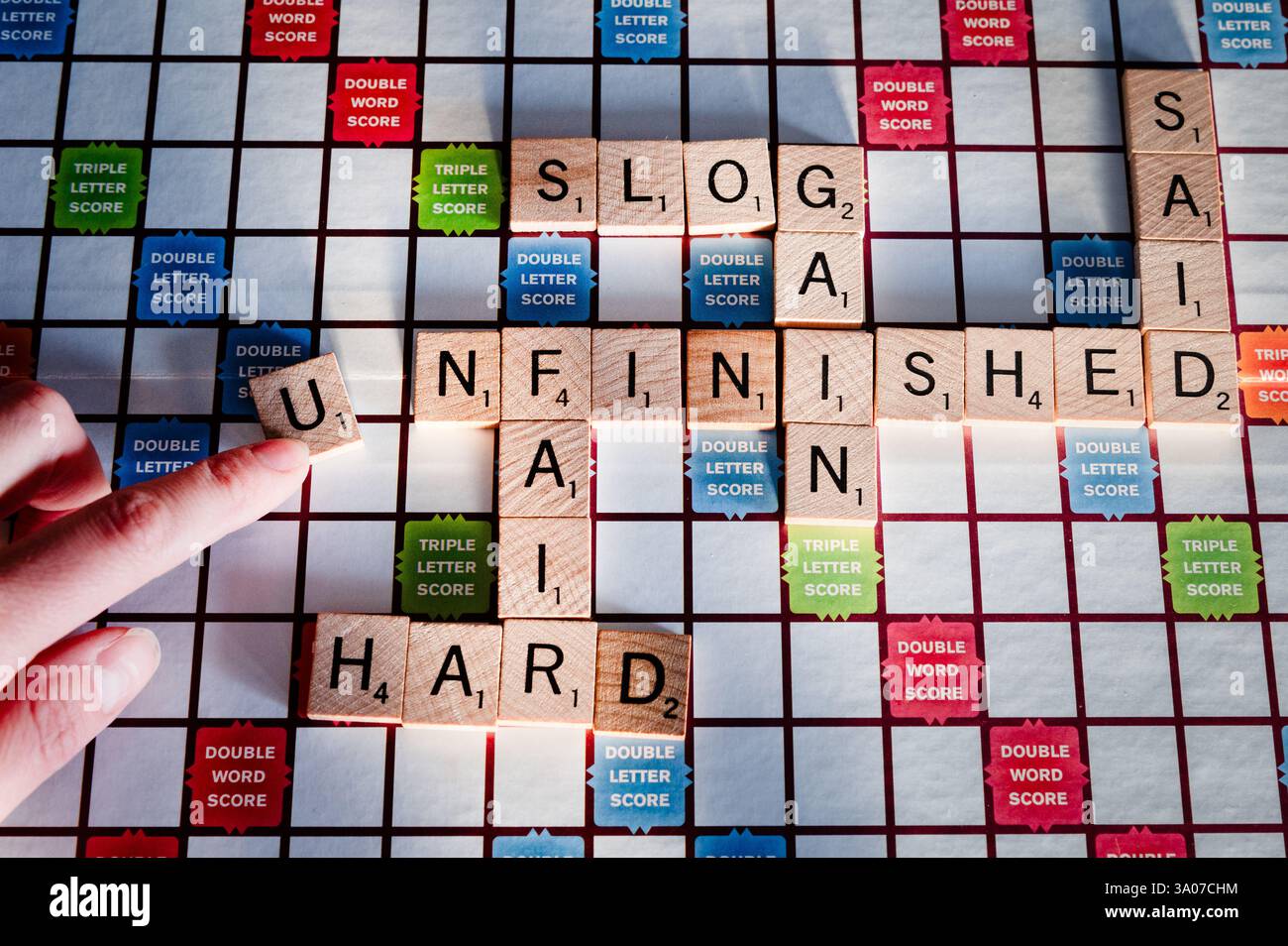 Un gioco Scrabble con una persona che crea la parola "incompiuto" Foto Stock