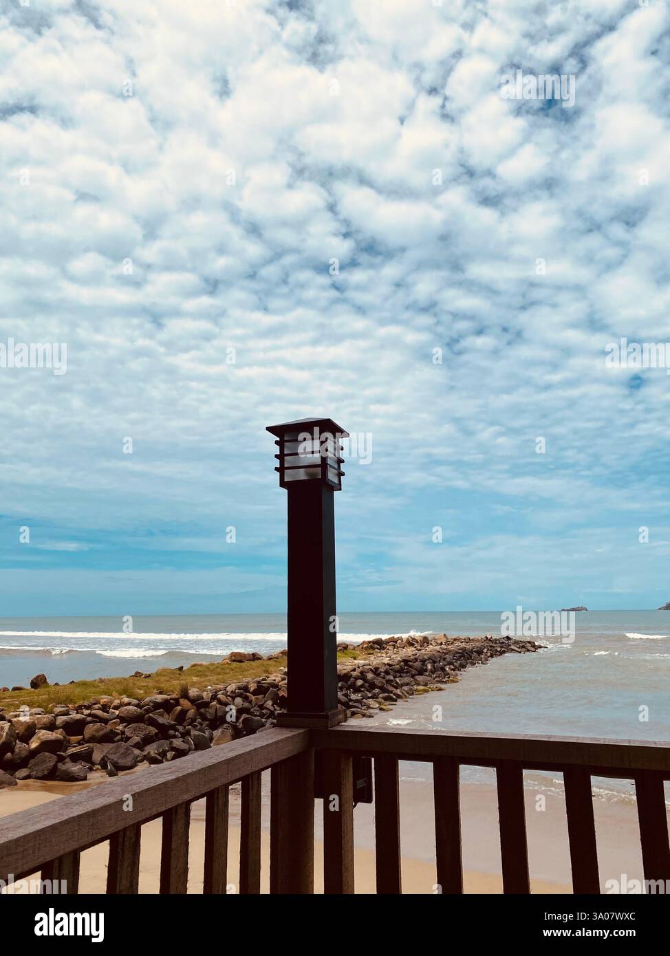 Una tranquilla vista sul mare con una formazione unica di nuvole, una ringhiera in legno e una lampada da giardino nera che creano una cornice perfetta per la bellezza dell'oceano. - Immagine stock catturata con smartphone