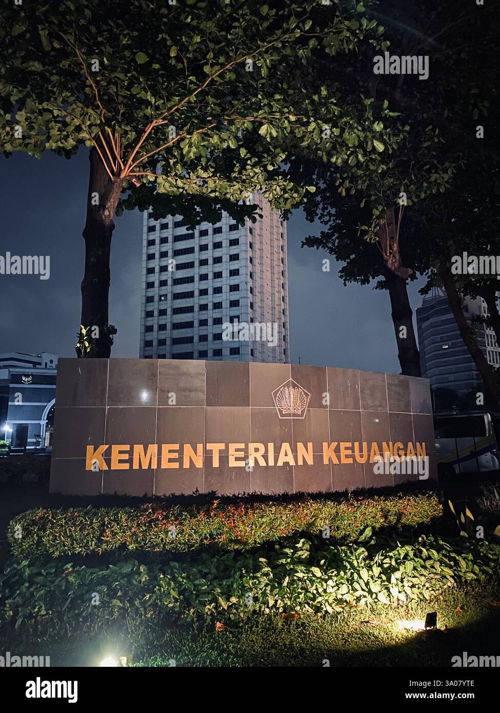 Una vista notturna del cartello del Ministero delle Finanze indonesiano, splendidamente illuminato e incorniciato da edifici torreggianti. Una potente rappresentazione del - Immagine stock catturata con smartphone
