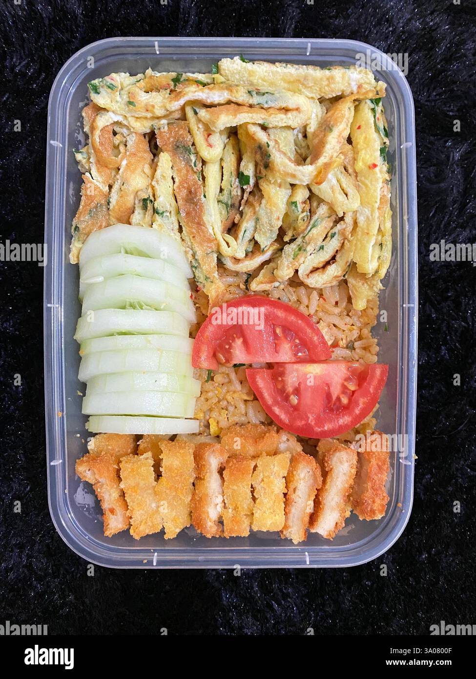 Un delizioso bento fatto in casa con croccante katsu di pollo, omelette alle erbe, riso fritto, cetriolo fresco e pomodori. Perfetto per preparare pasti e idee per il pranzo Foto Stock