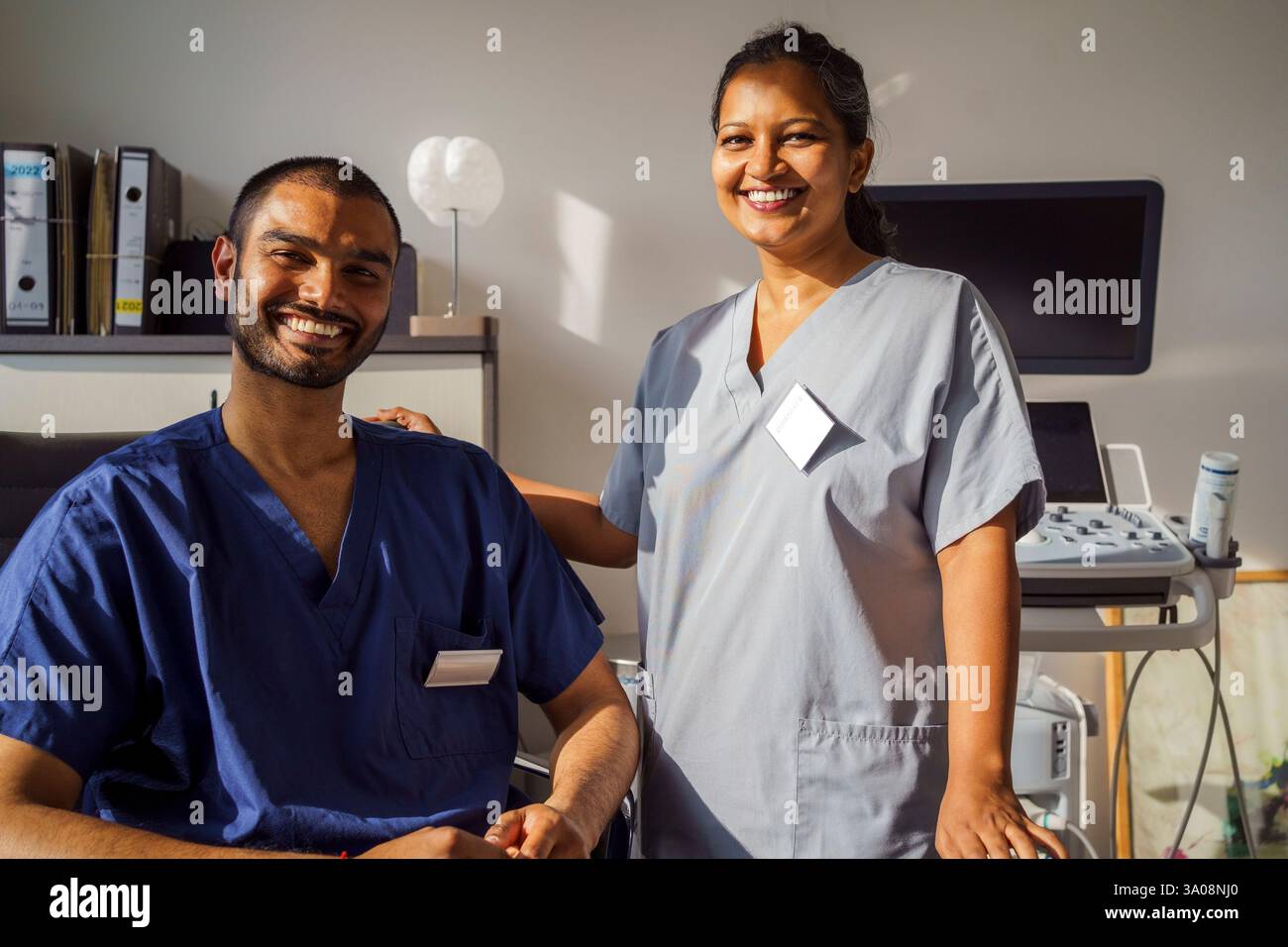Ritratto di lavoratrice sanitaria sorridente che indossa scrub medici in piedi vicino al collega maschio in clinica Foto Stock