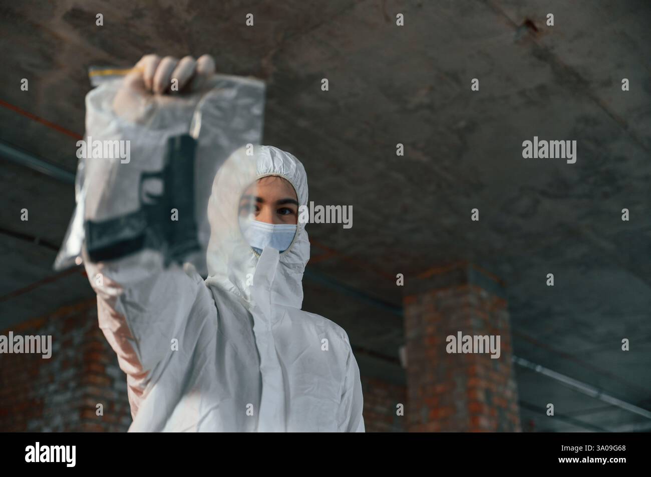 La donna con indumenti protettivi è al chiuso e tiene in mano la pistola. Prove di omicidio. Scena del crimine. Foto Stock