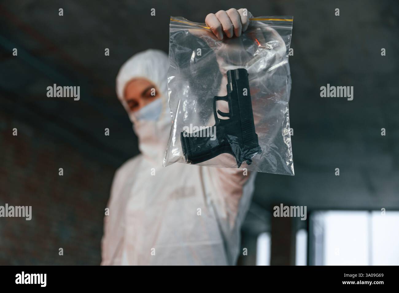 La donna con indumenti protettivi è al chiuso e tiene in mano la pistola. Prove di omicidio. Scena del crimine. Foto Stock