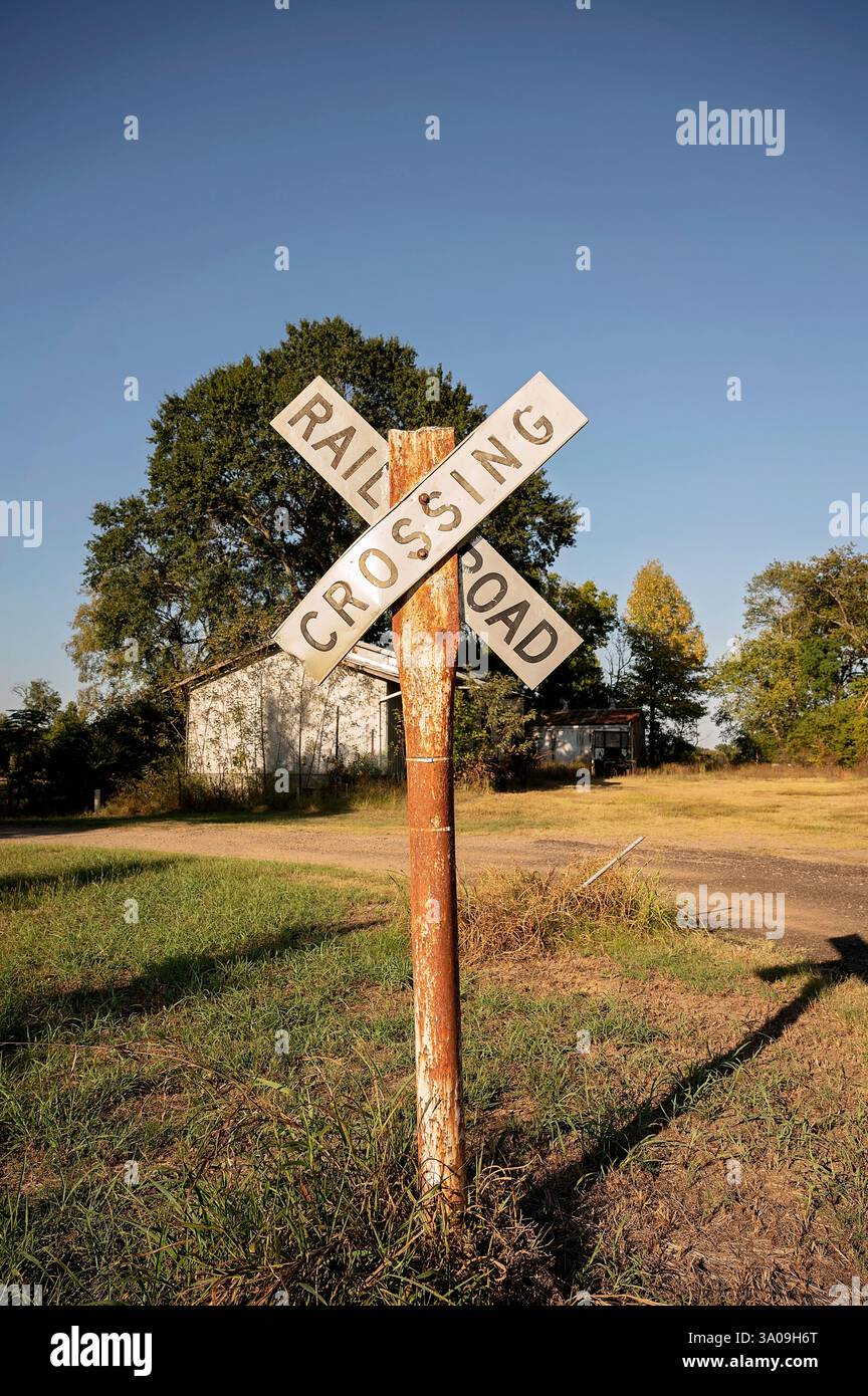 Segnaletica di attraversamento della ferrovia Rusty in un ambiente rurale con strade sterrate Foto Stock