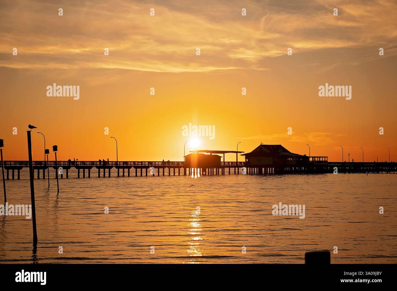 Molo sagomato al tramonto con riflessi dorati sull'acqua calma Foto Stock