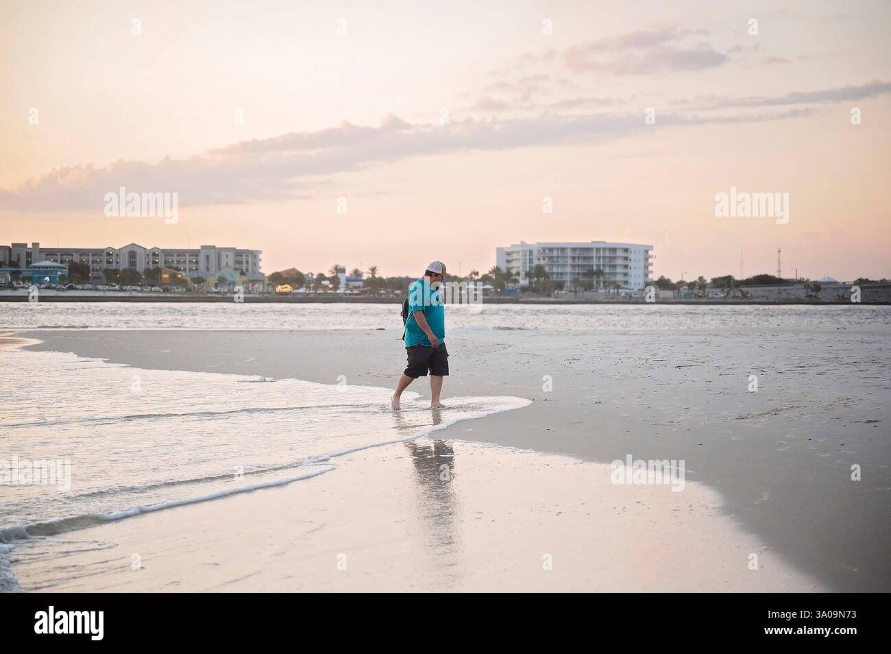 Uomo che cammina a piedi nudi lungo il litorale al tramonto con riflessi Foto Stock