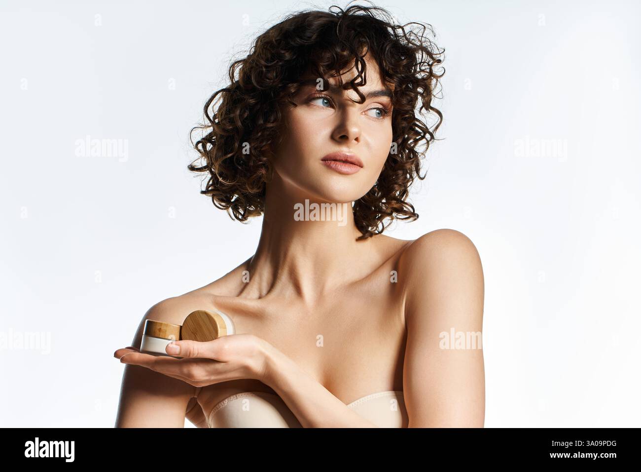 Una giovane donna mette in risalto la sua bellezza mentre tiene con grazia i cosmetici. Foto Stock