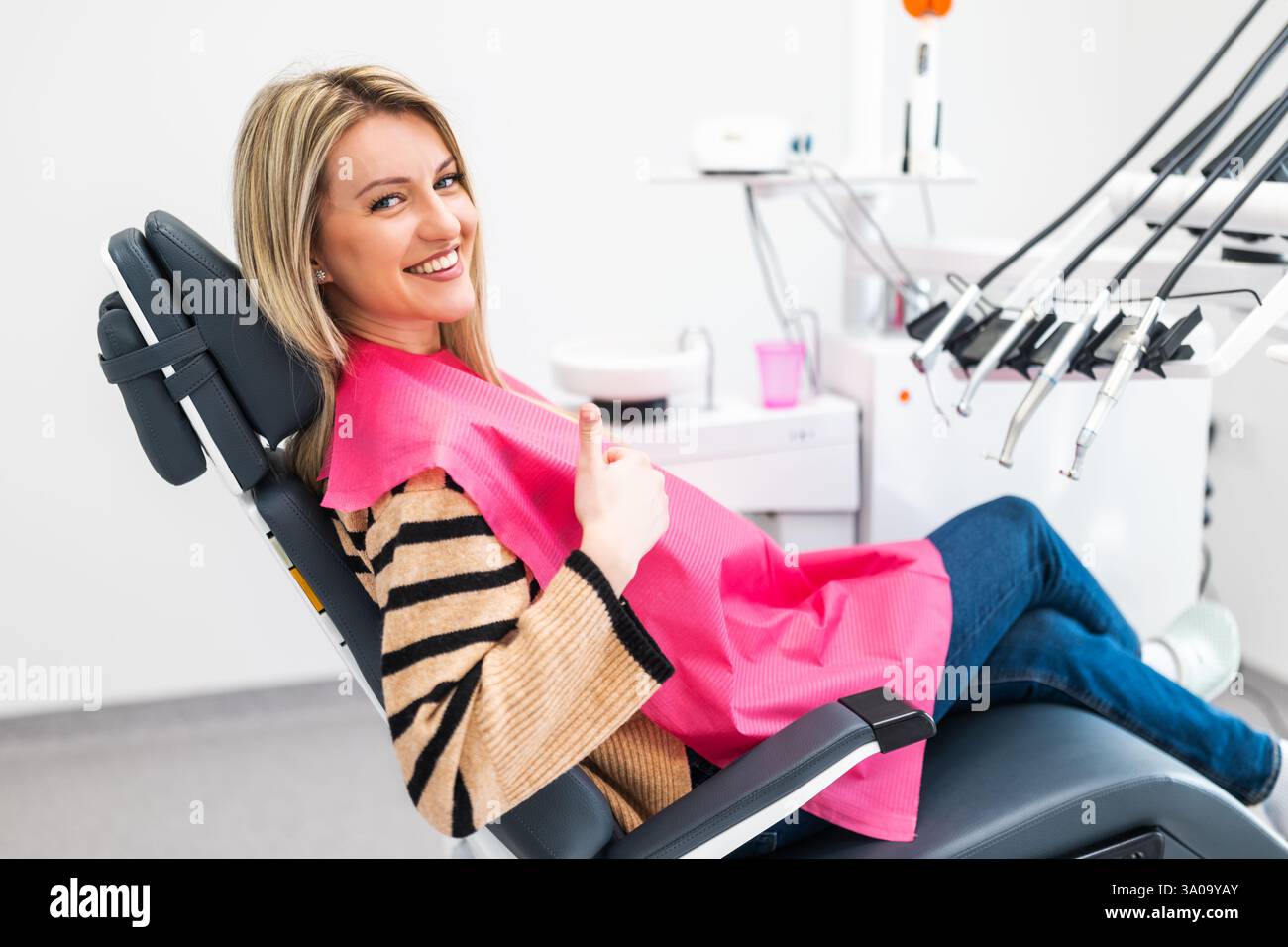 Giovane donna felice alla clinica odontoiatrica. Igiene e cura dentale professionale. Sta mostrando i pollici in alto. Foto Stock