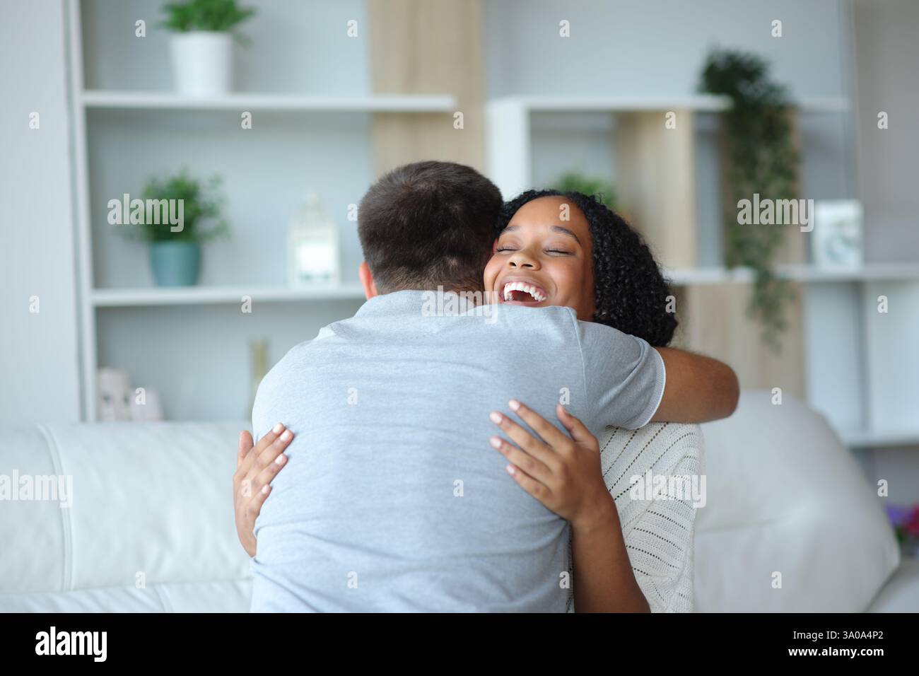 Donna nera felice che abbraccia un uomo seduto su un divano a casa Foto Stock