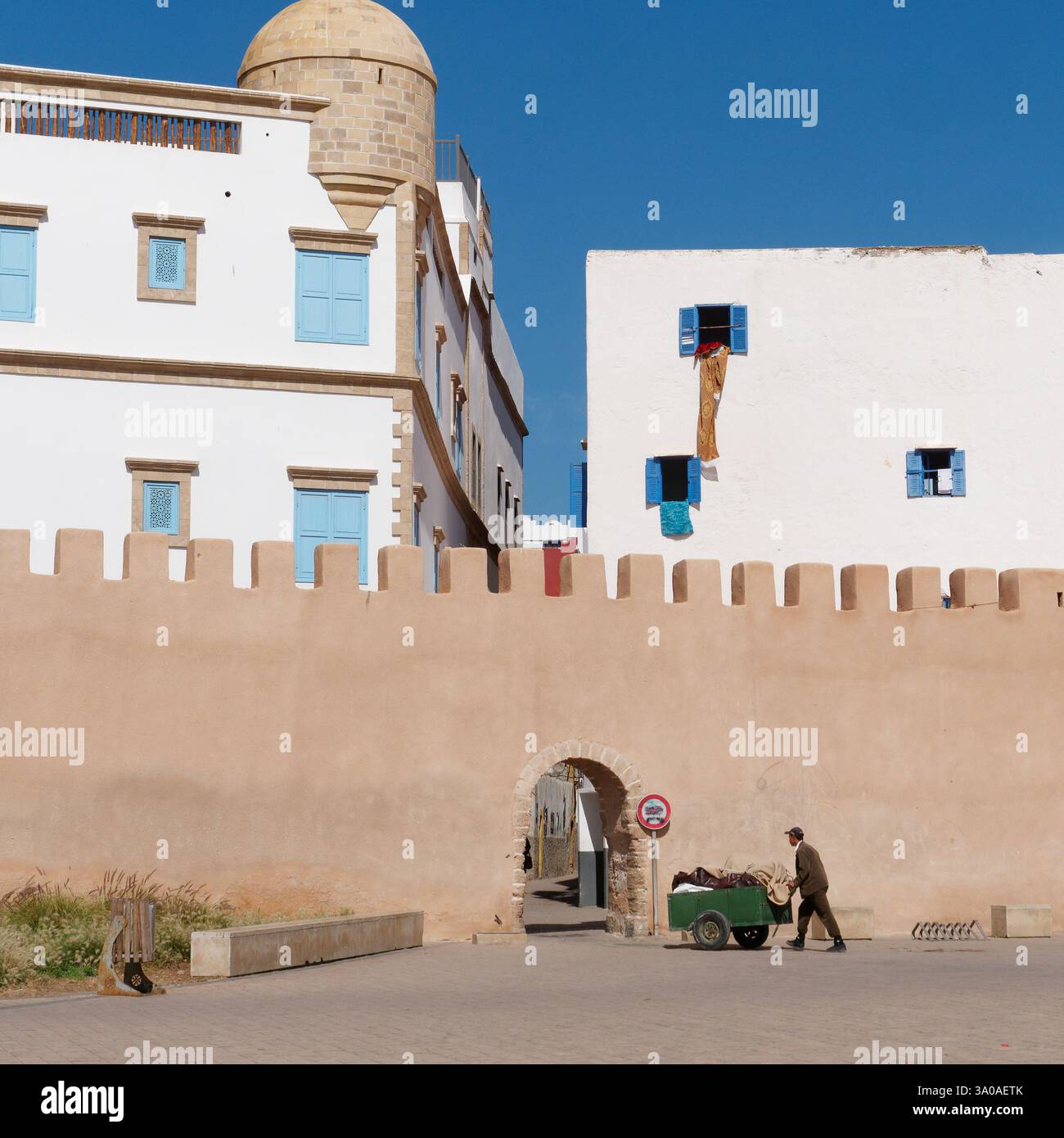 L'uomo spinge un carro verso un arco nelle mura della città di Medina come a Essaouira, in Marocco. 2 marzo 2025 Foto Stock