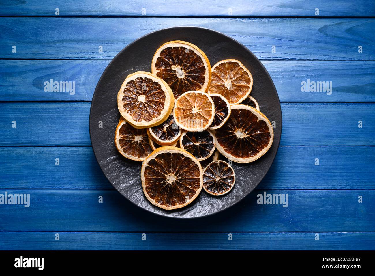 Fette di agrumi essiccate in piatto nero su un tavolo rustico in legno blu. Fotografia gastronomica Foto Stock