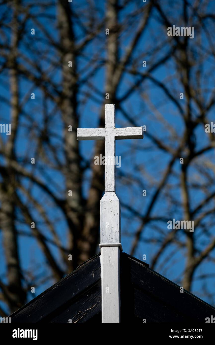 Croce di legno dipinta di bianco luminoso con uno sfondo di alberi fuori fuoco. Foto Stock
