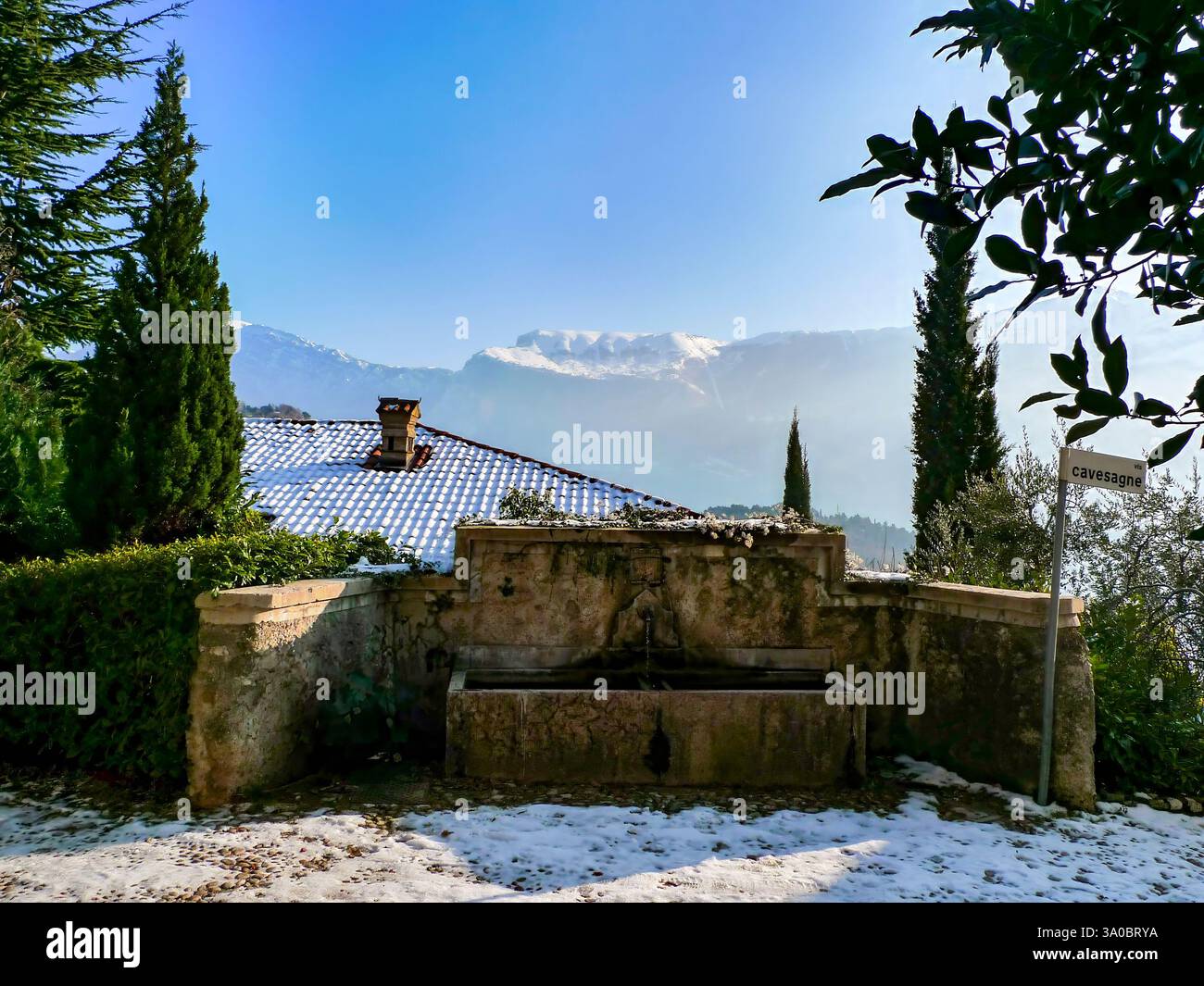 La fontana del paese a Musio in inverno. Il Monte Baldo innevato sullo sfondo. Musio è un distretto di Tremosine sulla riva occidentale del lago Foto Stock