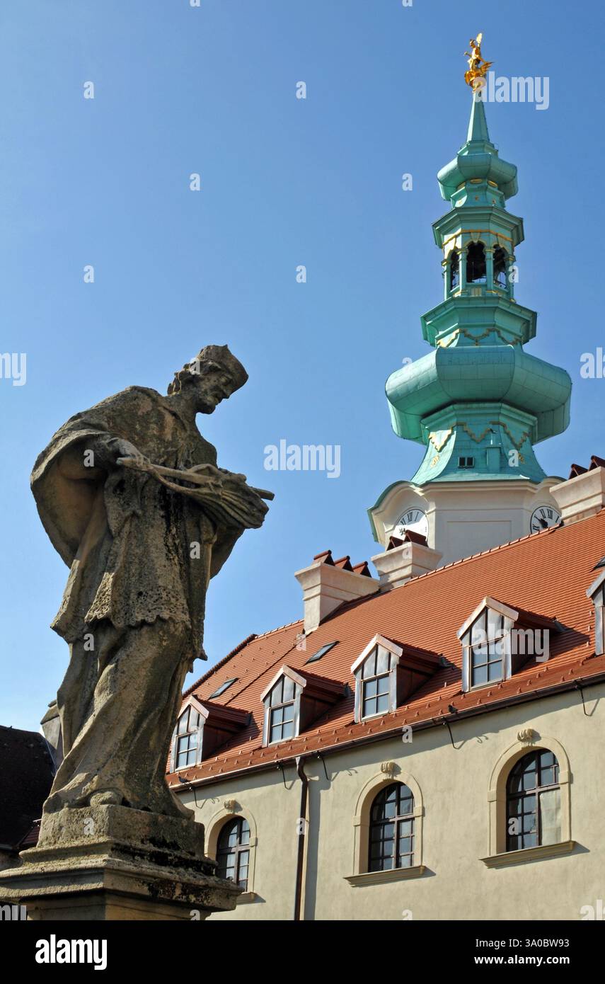 Una statua sorge su un ponte sotto la torre della porta di Michele nella storica città vecchia di Bratislava. Foto Stock