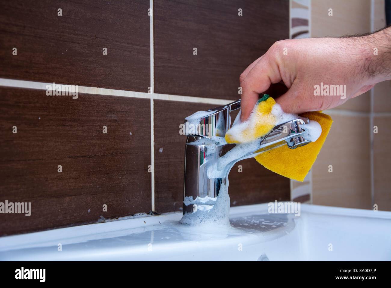 Una mano maschile irriconoscibile senza guanti pulisce il rubinetto del bagno Foto Stock