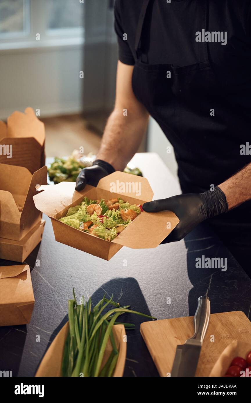 L'uomo sta imballando il cibo nelle scatole ecologiche di carta. All'interno, ristorante. Foto Stock