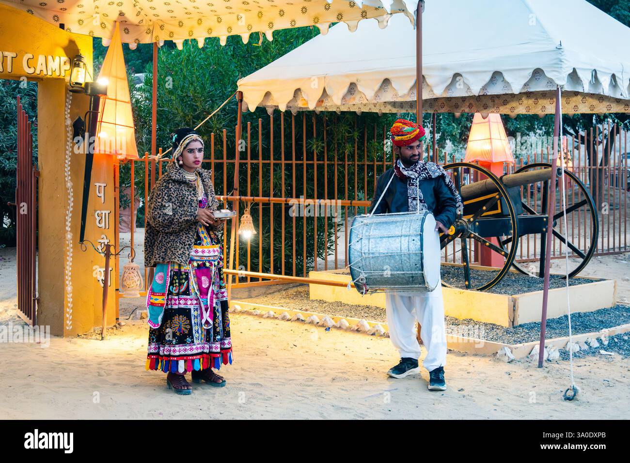 Un uomo e una donna in abito tradizionale accolgono gli ospiti in un accampamento nel deserto. Rajasthan, India. Foto Stock