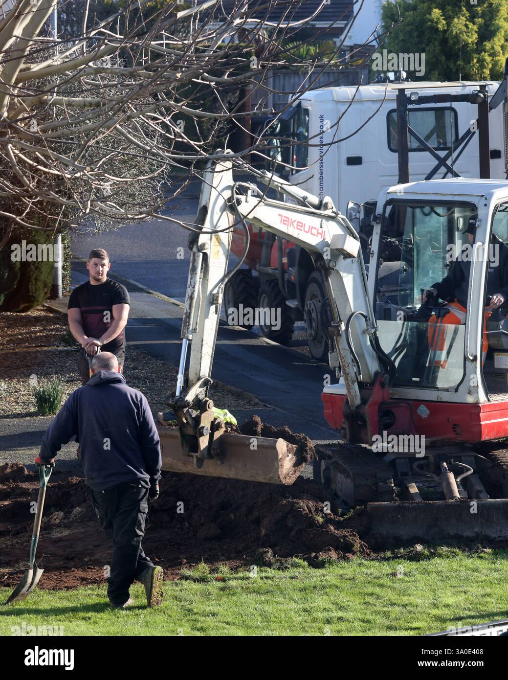 Febbraio 2025 - uomini appoggiati sulle pale che guardano una piccola scavatrice al lavoro Foto Stock