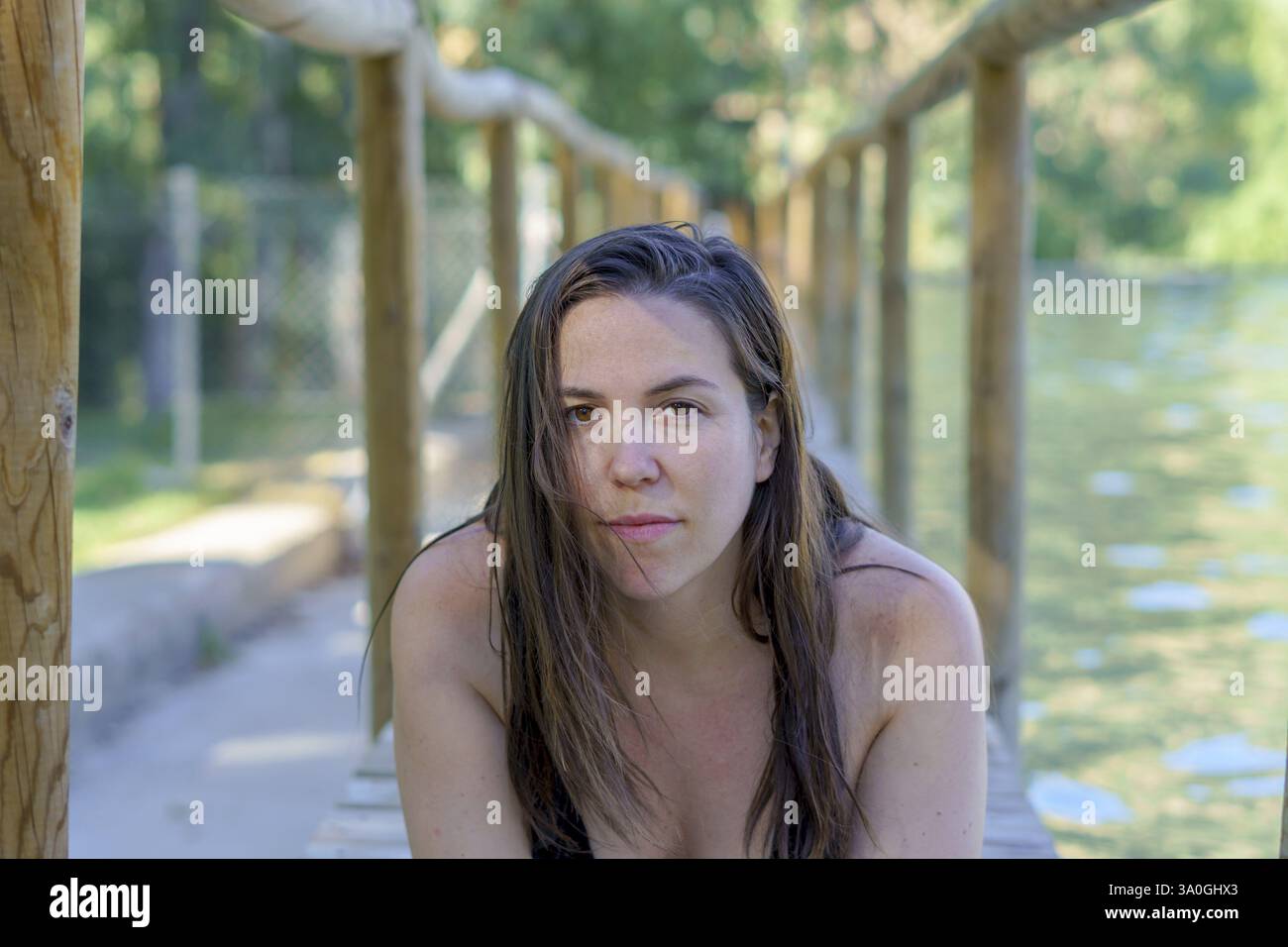 Primo piano di una bella donna bruna in costume da bagno distesa su un pontile di legno su un lago che guarda la macchina fotografica Foto Stock