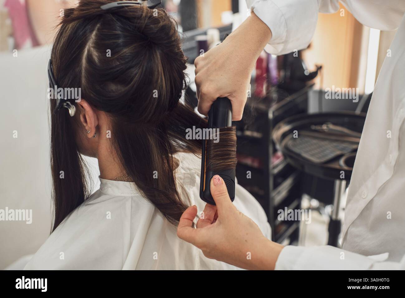 Il processo di arricciatura dei capelli con un ferro da stiro professionale in un salone di bellezza. Acconciatura in primo piano. Foto Stock