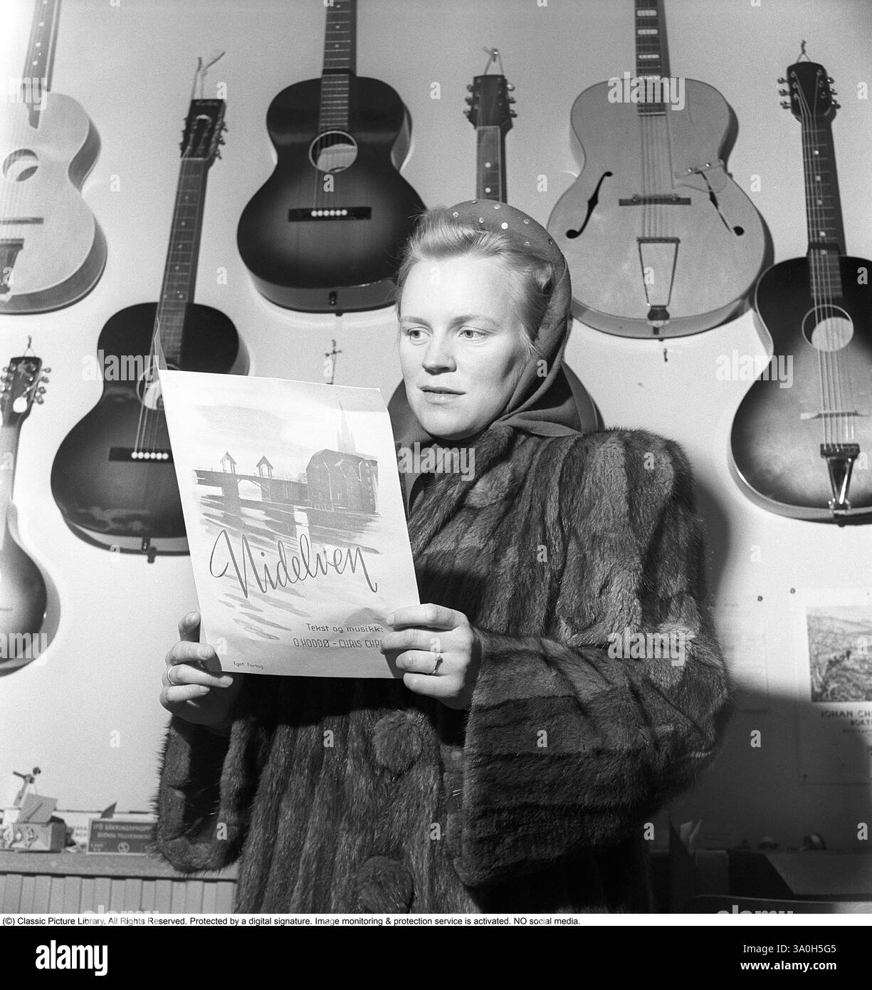 Inger Hoddø. Moglie di Oskar Hoddø (1916-1943) è stata una cantante norvegese, compositore e combattente della resistenza. Hoddø è meglio conosciuto per aver scritto il testo del valzer «Nidelven stille og vakker du er». La canzone fu un successo locale a Trondheim per molto tempo, ma divenne un successo in tutto il mondo. Inger Hoddø è fotografato nel negozio di musica di Kjell Rian a Trondheim. Kjell è stato quello che ha arrangiato la melodia e l'ha fatta registrare. Inger ha in mano un libretto di spartiti con Nidelven e un'illustrazione di Den gamle bybro a Trondheim sul davanti. Kristoffersson rif. AU42-1 Foto Stock