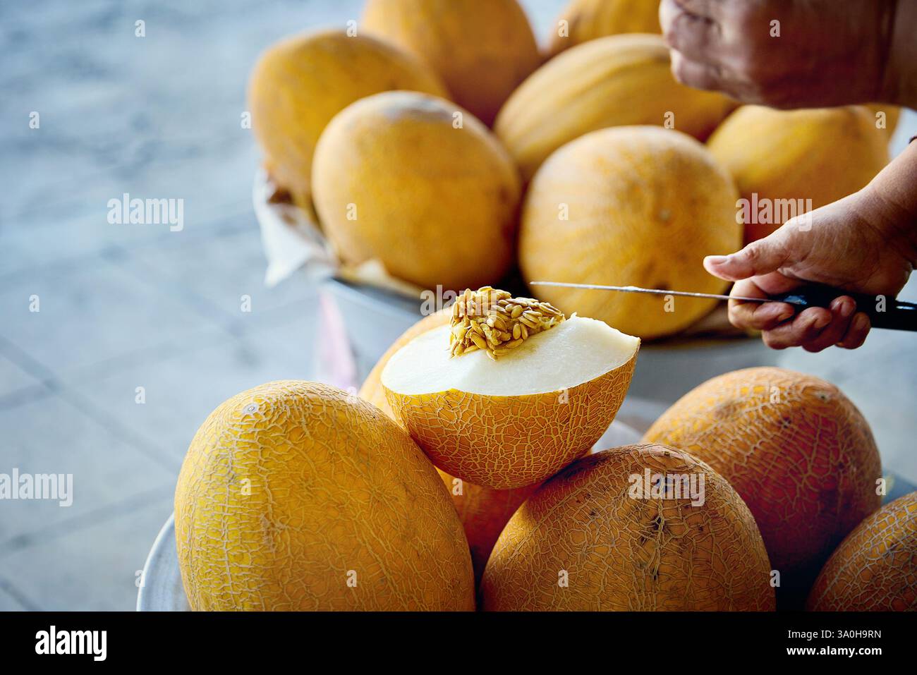 L'uomo ha tagliato il melone uzbeko giallo maturo con un coltello al Market bazar di Bukhara, Uzbekistan Foto Stock