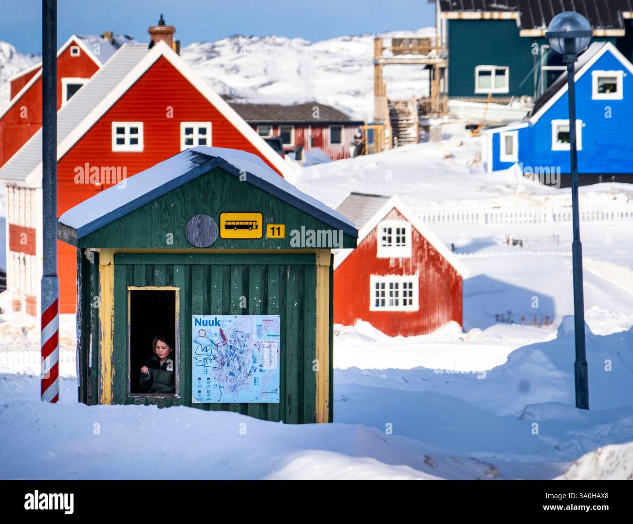 Una colorata scena invernale a Nuuk, in Groenlandia, caratterizzata da un piccolo capannone verde con una persona all'interno, circondato da edifici innevati dai colori vivaci. Foto Stock
