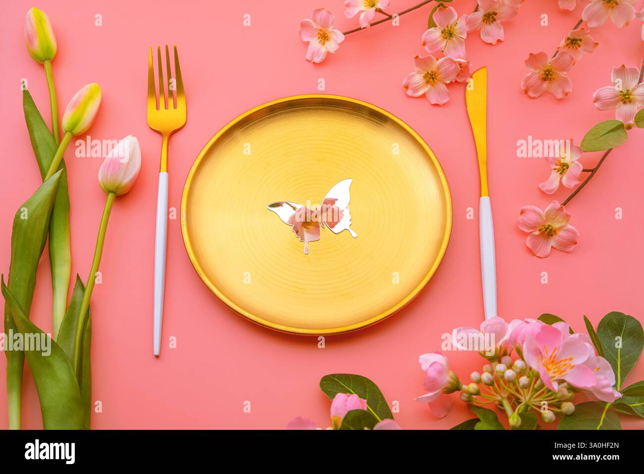 Piatto dorato decorato con farfalla a specchio, che riflette il fiore rosa della primavera, i tulipani rosa e i fiori di ciliegio creando una vibrante composizione primaverile Foto Stock