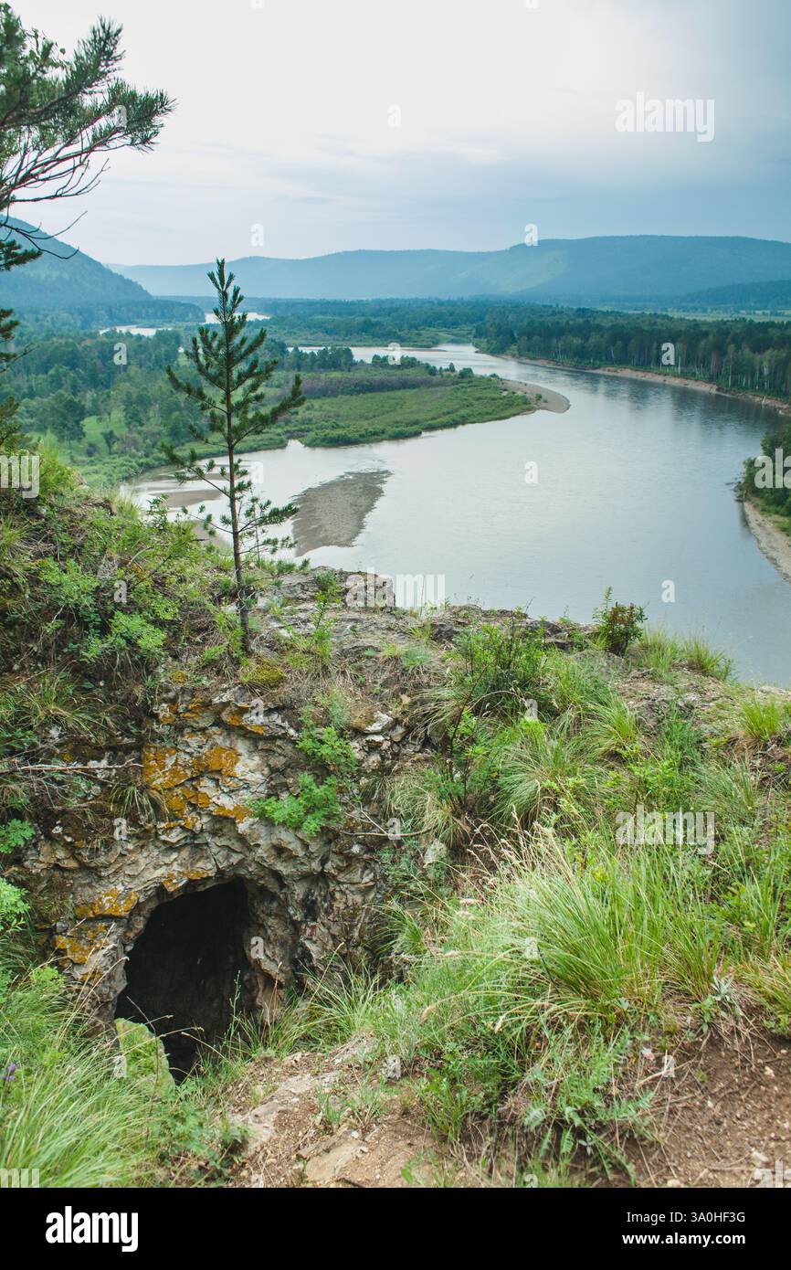 Vista panoramica da una scogliera che si affaccia su un fiume, circondato da vegetazione lussureggiante e da una grotta di roccia naturale in una giornata nuvolosa Foto Stock