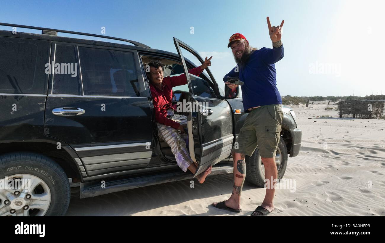 Due turisti posano giocosamente vicino a un veicolo nell'ambiente sabbioso dell'isola di Socotra, condividendo un momento di gioia insieme. Foto Stock