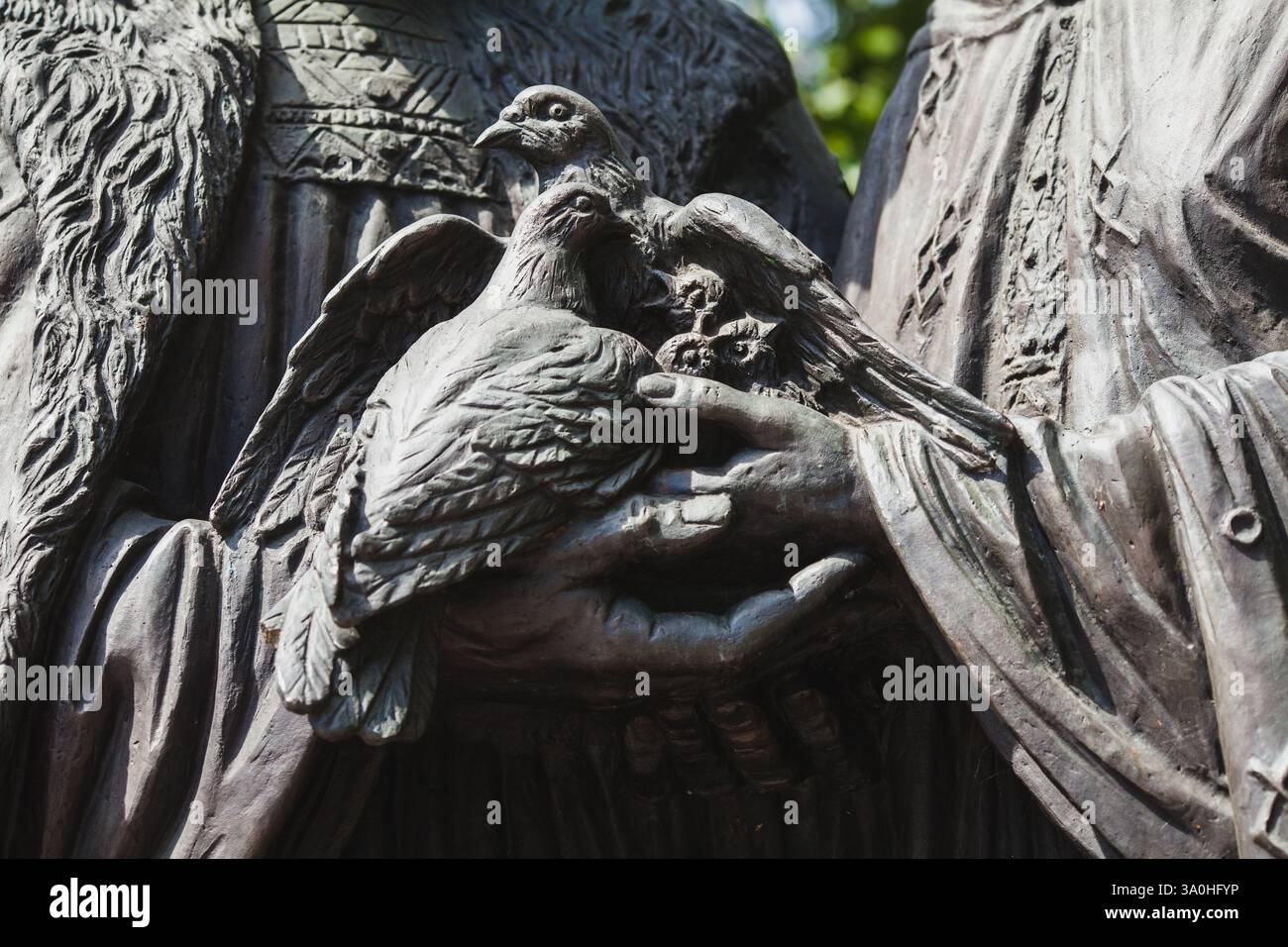 Una dettagliata scultura in bronzo a due mani che reggono dolcemente un paio di colombe, simboleggiando la pace e l'unità in una giornata nuvolosa Foto Stock