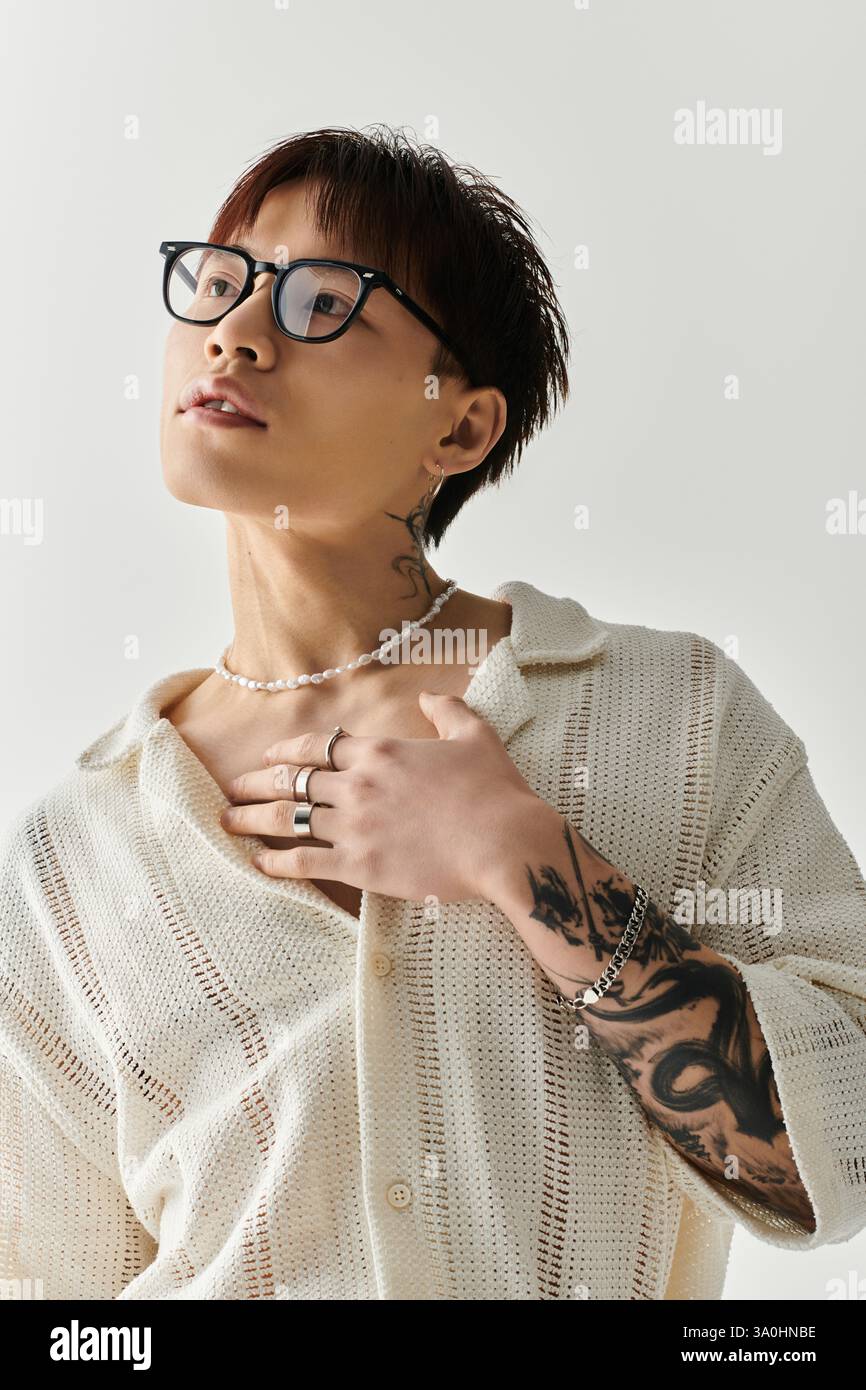 Un giovane uomo asiatico alla moda con tatuaggi e occhiali mette in mostra il suo stile unico e la sua fiducia. Foto Stock