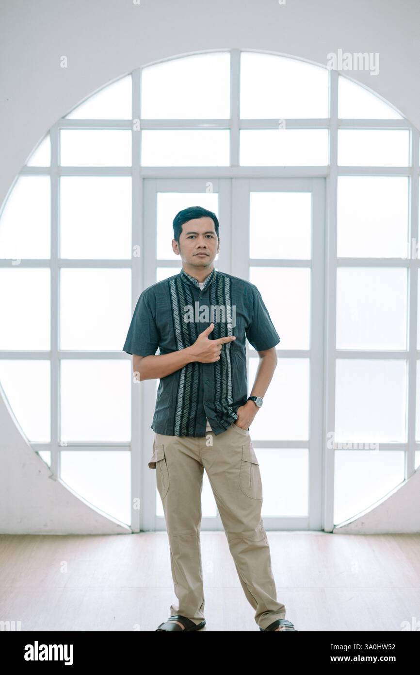 Un uomo con un abbigliamento casual, in piedi all'interno con un look sicuro e puntato verso uno spazio vuoto. Indossa una camicia elegante e una t marrone chiaro Foto Stock