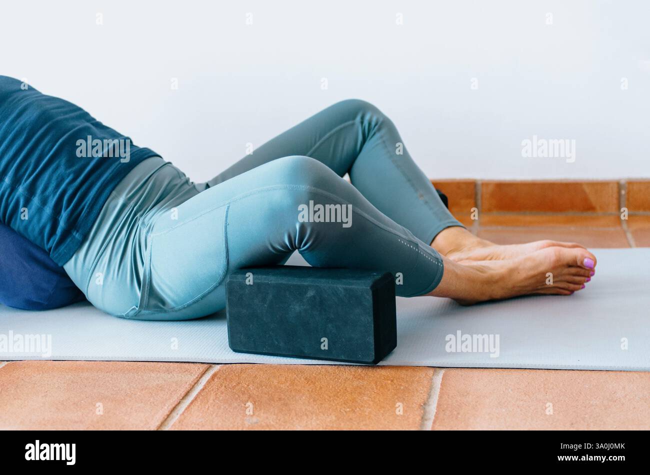 Parte inferiore del corpo della donna che pratica yoga rigenerante, ginocchia sostenute da blocchi Foto Stock