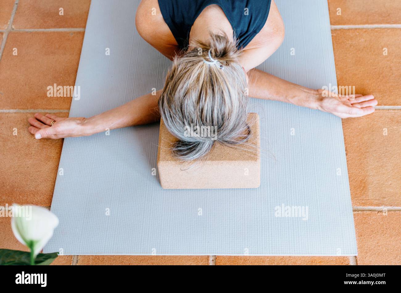 Donna che pratica yin yoga allungamento del braccio incrociato, testa sostenuta da un blocco di sughero Foto Stock