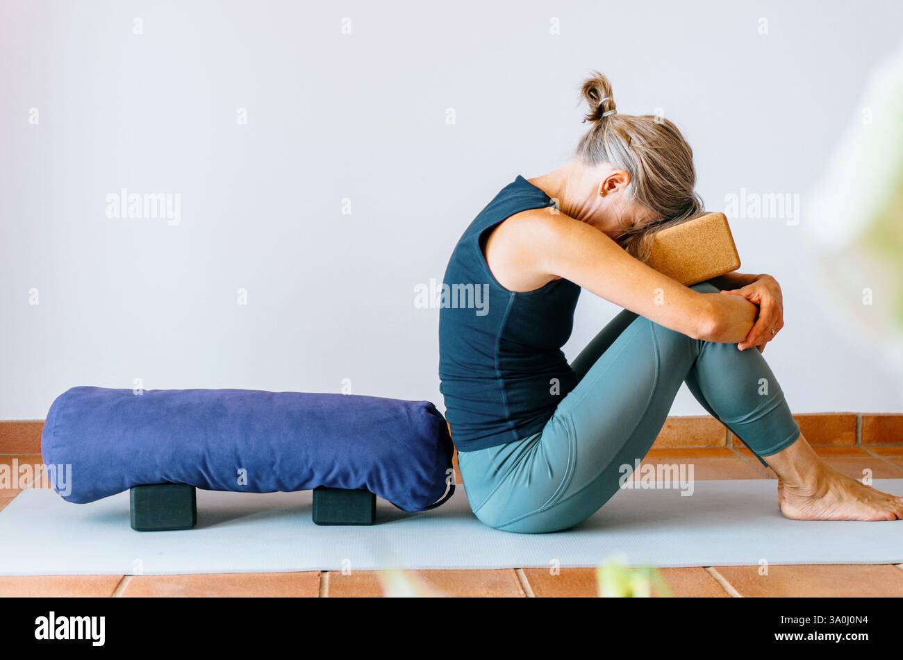 Donna seduta seduta in posa yoga autolubrificante con la fronte appoggiata su un blocco Foto Stock