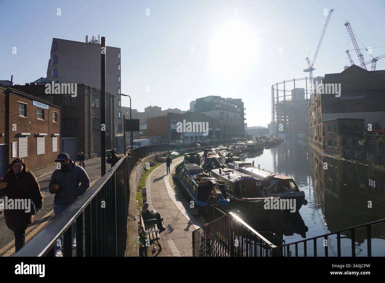 La vista del sentiero sul Regent's Canal al sole del mattino presto della primavera. Le barche della casa costeggiano il canale con i lavori di costruzione alle spalle. Foto Stock